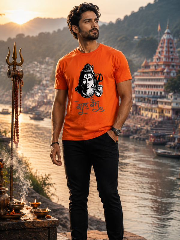 Model in Zingleberry saffron orange Bol Bam t-shirt with Lord Shiva face artwork and trishul, standing in front of decorated Shiva temple
