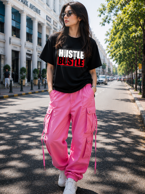 Female model wearing Zingleberry Hustle Bustle Premium Unisex Black Cotton Graphic T-Shirt styled with pink cargo pants for a trendy summer streetwear outfit.