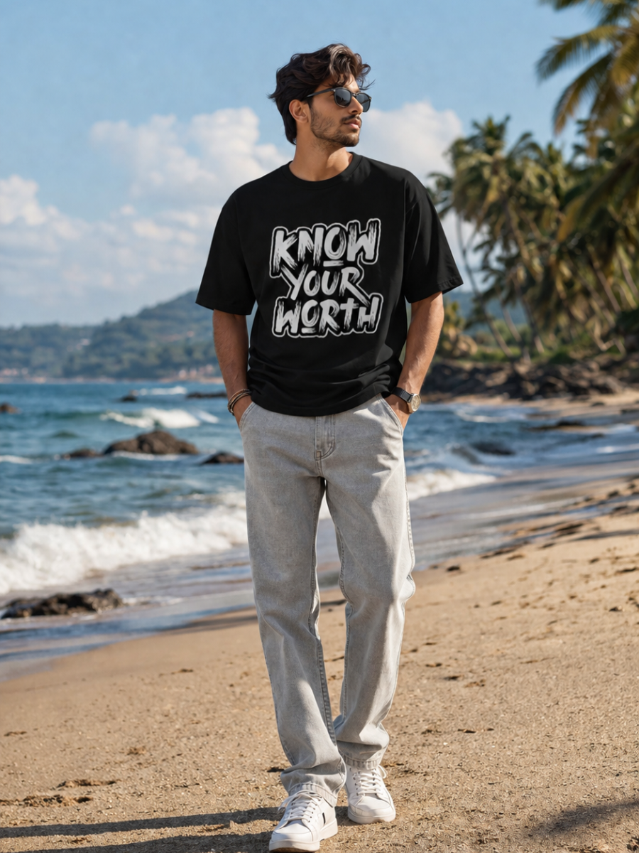Male model wearing Zingleberry Know Your Worth Premium Black Cotton Graphic T-Shirt paired with light grey jeans for a stylish beachside casual streetwear look.