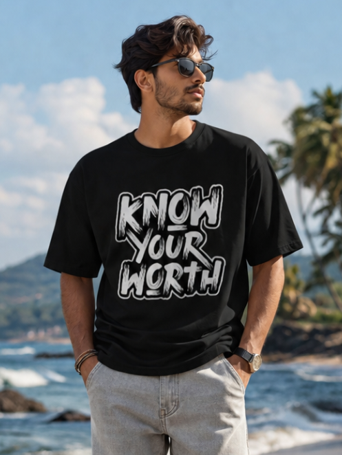 Male model wearing Zingleberry Know Your Worth Premium Black Cotton Graphic T-Shirt paired with light grey jeans for a stylish beachside casual streetwear look.