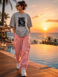 female model wearing a gray zingleberyy's oversized unisex t-shirt with text and pink cargo pants standing by a pool with a sunset view.