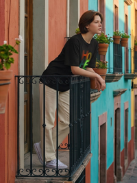 female model with Zingleberry Cooton Hope Printed tshirt leaning on a balcony railing with colorful buildings in the background