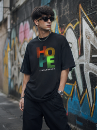 Person wearing a Zingleberry Cotton black t-shirt with colorful text in front of a graffiti-covered wall.