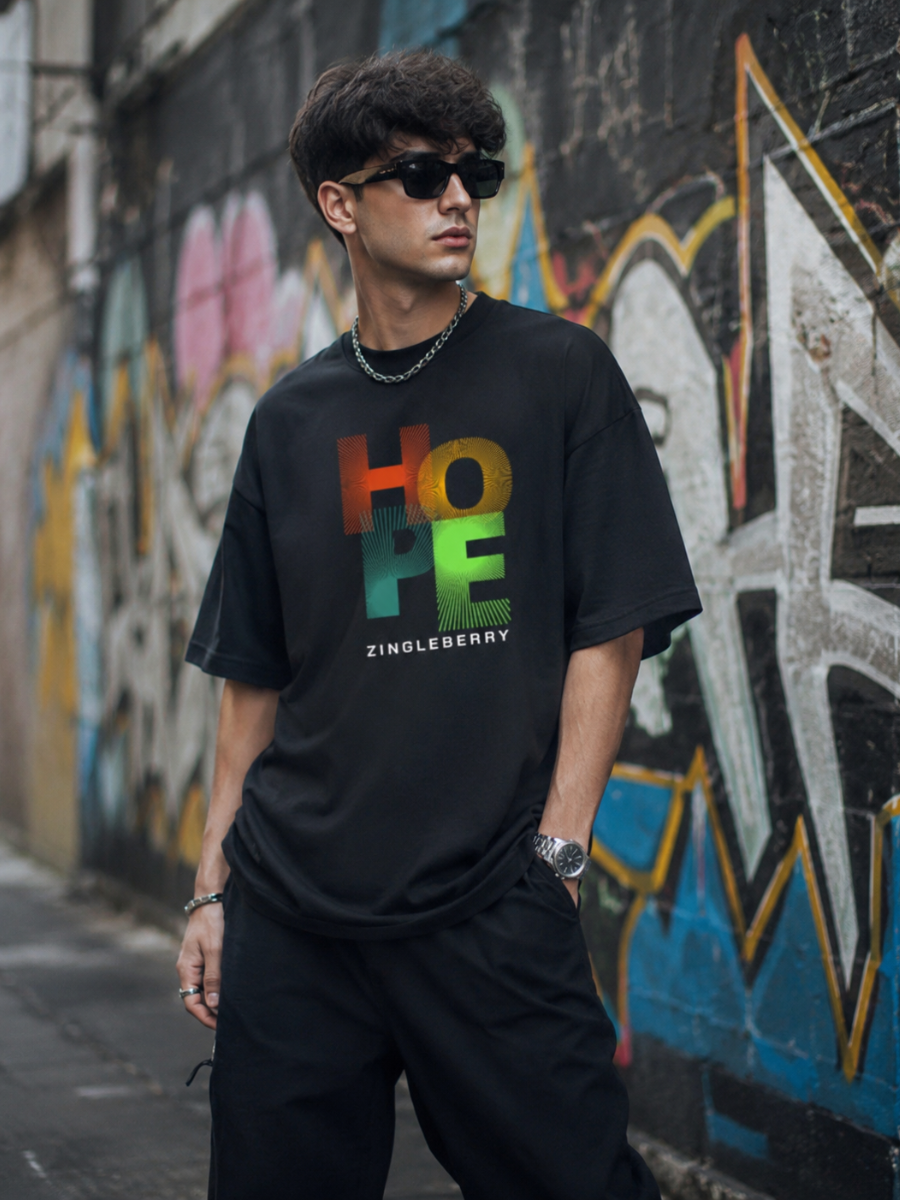 Person wearing a Zingleberry Cotton black t-shirt with colorful text in front of a graffiti-covered wall.