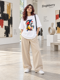 Woman wearing Zingleberry white Art in Motion oversized graphic T-shirt with beige wide-leg trousers.