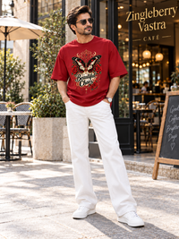 Man wearing Zingleberry Beautiful Chaos red oversized graphic T-shirt with white relaxed trousers outside a premium café.