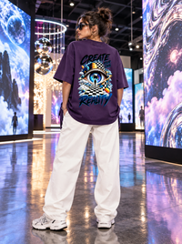 Female model wearing Zingleberry Create Your Own Reality purple oversized graphic T-shirt with white wide-leg pants at a digital art exhibition.