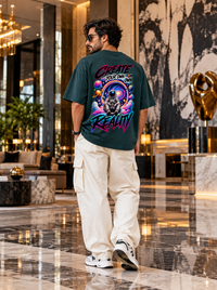 Male model showcasing Zingleberry Create Your Own Reality petrol blue oversized T-shirt with large neon astronaut galaxy artwork and off-white cargo trousers in premium interior