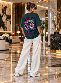 Female model wearing Zingleberry Create Your Own Reality dark green oversized T-shirt with vibrant astronaut back artwork, cream wide-leg trousers and white sneakers in luxury interior