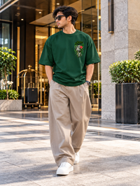 Man wearing Zingleberry Grow Through It premium bottle green oversized cotton T-shirt with botanical left-chest graphic.