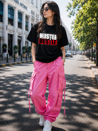 Female model wearing Zingleberry Hustle Bustle Premium Unisex Black Cotton Graphic T-Shirt styled with pink cargo pants for a trendy summer streetwear outfit.