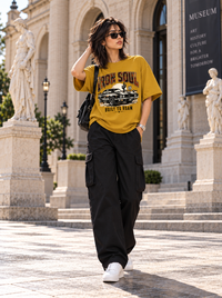 Female model wearing Zingleberry Iron Soul mustard yellow oversized graphic T-shirt with black cargo trousers and white sneakers.