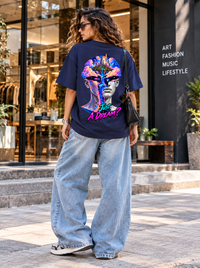 Female model wearing Zingleberry Just A Dream navy blue oversized T-shirt featuring vibrant surreal portrait and floating dream kingdom artwork with light-wash wide-leg jeans