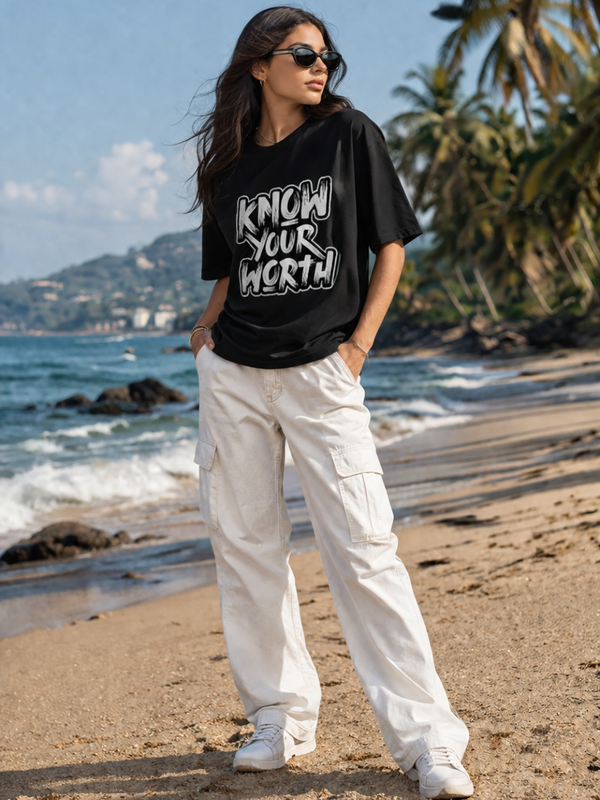 Female model wearing Zingleberry Know Your Worth Premium Unisex Black Cotton Graphic T-Shirt styled with white cargo pants for a trendy beach-inspired summer streetwear outfit.