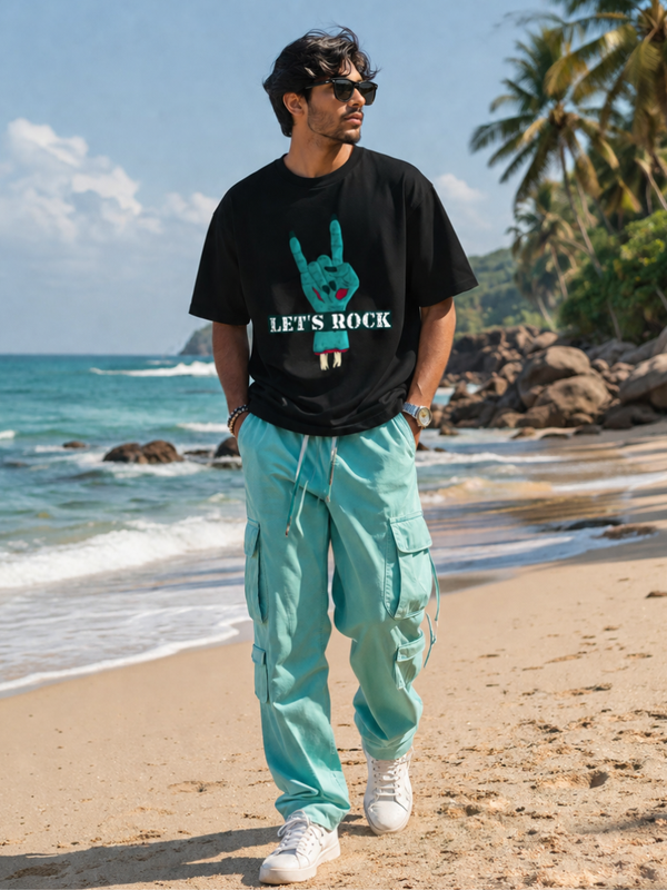 Male model wearing Zingleberry Let's Rock Premium Unisex Black Cotton Graphic T-Shirt with turquoise cargo pants for a stylish summer streetwear look.