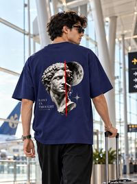 Back view of male model wearing Zingleberry Lost in Thought navy blue oversized graphic T-shirt with classical statue and moon artwork.