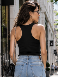 Back view of female model wearing a plain black Zingleberry women’s tank top with light blue jeans in an urban street setting.