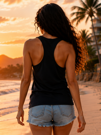 Back view of female model wearing a plain navy blue Zingleberry women’s tank top with denim shorts on a sunset beach.