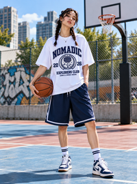 Female model wearing Zingleberry Nomadic Explorers Club white oversized T-shirt with navy basketball shorts and white sneakers.