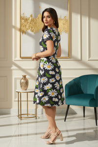 Woman in a zingleberry's A line  black and white daisy floral dress standing stylish three-quarter angle (partially showing the back and one side of the face) in a stylish room with a teal chair and gold decor.