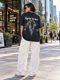 Female model wearing Zingleberry Rhythm Energy Mode black oversized T-shirt featuring monochrome futuristic runner back artwork with white cargo trousers and sneakers