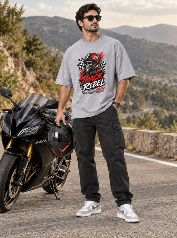 Male model wearing Zingleberry Track Rebel grey oversized biker graphic T-shirt with black cargo jeans beside a sport motorcycle on a scenic mountain road.